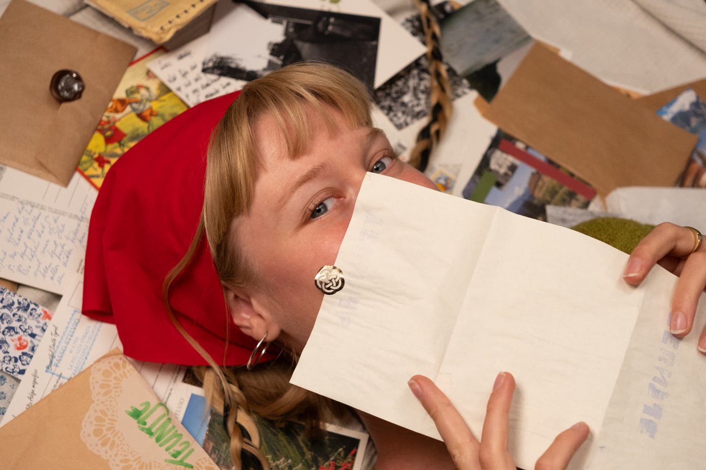 The founder lying among postcards and letters, holding a letter in front of her face